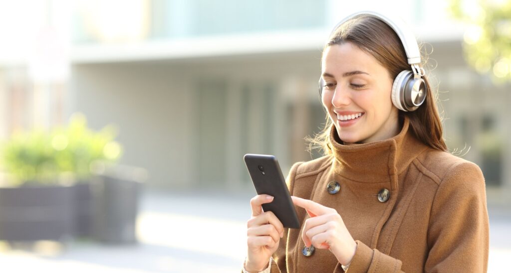 Ragazza cammina con cuffie a padiglione e cellulare in mano